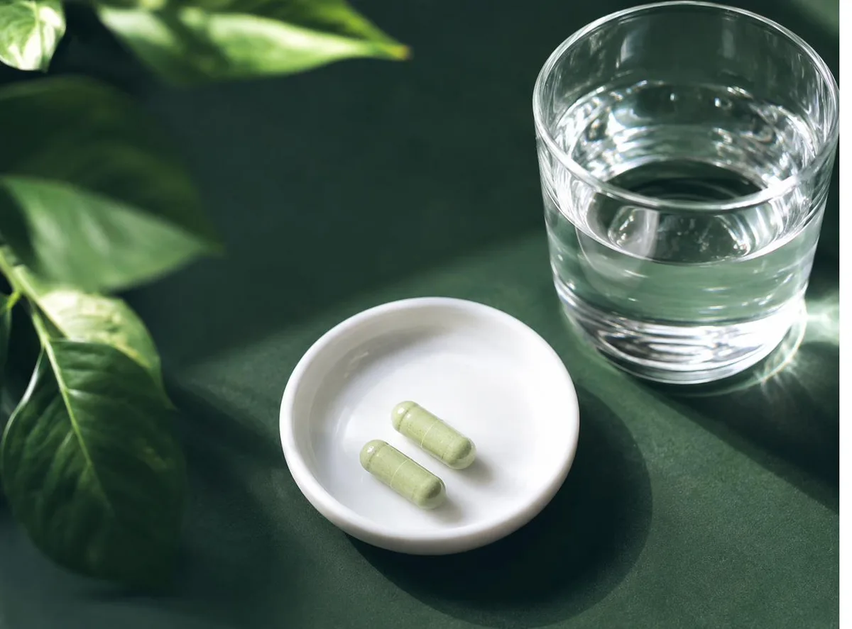 Two compounded capsules on a small white tray beside a glass of water